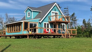Een tweelaags huis met een houten terras en balkon, omringd door een grasveld en bomen.