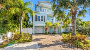A two-story house with a light blue exterior, a front driveway, and surrounding tropical vegetation.