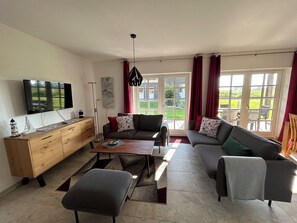 Uma sala de estar moderna com um sofá, um banquinho, uma mesa de centro e uma TV fixada na parede.