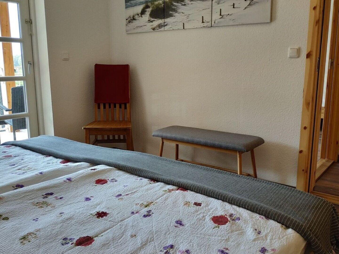 A bedroom with a bed, a bench, a chair, and a painting on the wall.