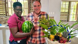 Two people standing in a room with a kitchen counter, a window with blinds, and a basket of fruits and vegetables. - Reef Utopia Tobago Private Beautiful Villa,3mins Walk to Beach,Great Pool,Garden (Tobago)