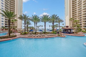 A large swimming pool surrounded by palm trees and lounge chairs, with high-rise buildings in the background. - Shores of Panama studio - Gulf views (Panama City Beach)