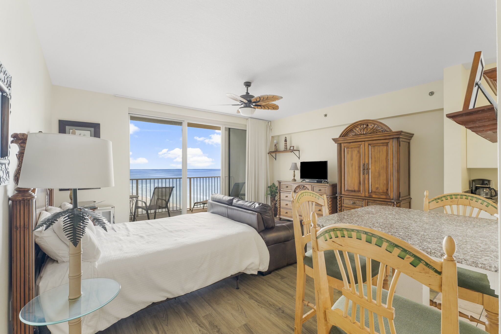 A bedroom with a bed, a desk, a chair, a television, and a view of the ocean.