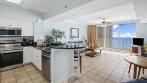 Una cocina moderna con una isla central, un comedor con vistas al balcón, y una sala de estar con un amplio ventanal con vista al océano.