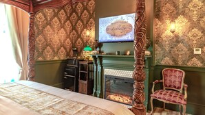 A bedroom with a four-poster bed, a green fireplace, a television, and a decorative chair.