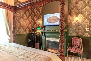A bedroom with a four-poster bed, a green fireplace, a television, and a decorative chair.