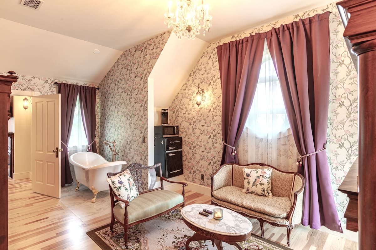 A room with a clawfoot bathtub, a vintage sofa, a marble coffee table, and a chandelier.
