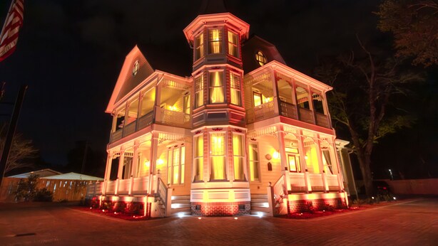 A large, multi-story building with a prominent tower and multiple windows, illuminated at night.