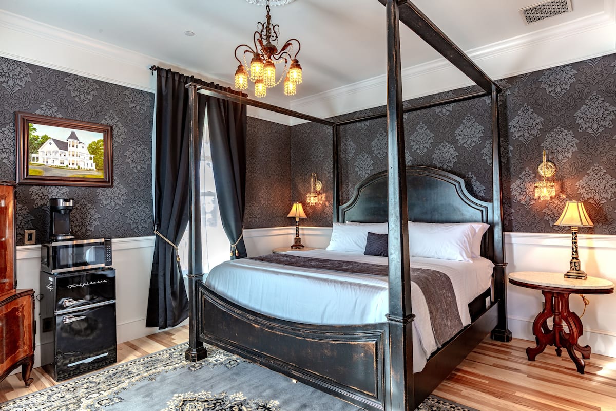 A four-poster bed with a dark headboard, a chandelier, and two bedside tables with lamps.