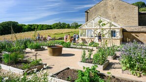 A garden with raised beds, a large planter, and a building with a gabled roof. - 4 bedroom accommodation in Broughton, near Skipton (Broughton, near Skipton)