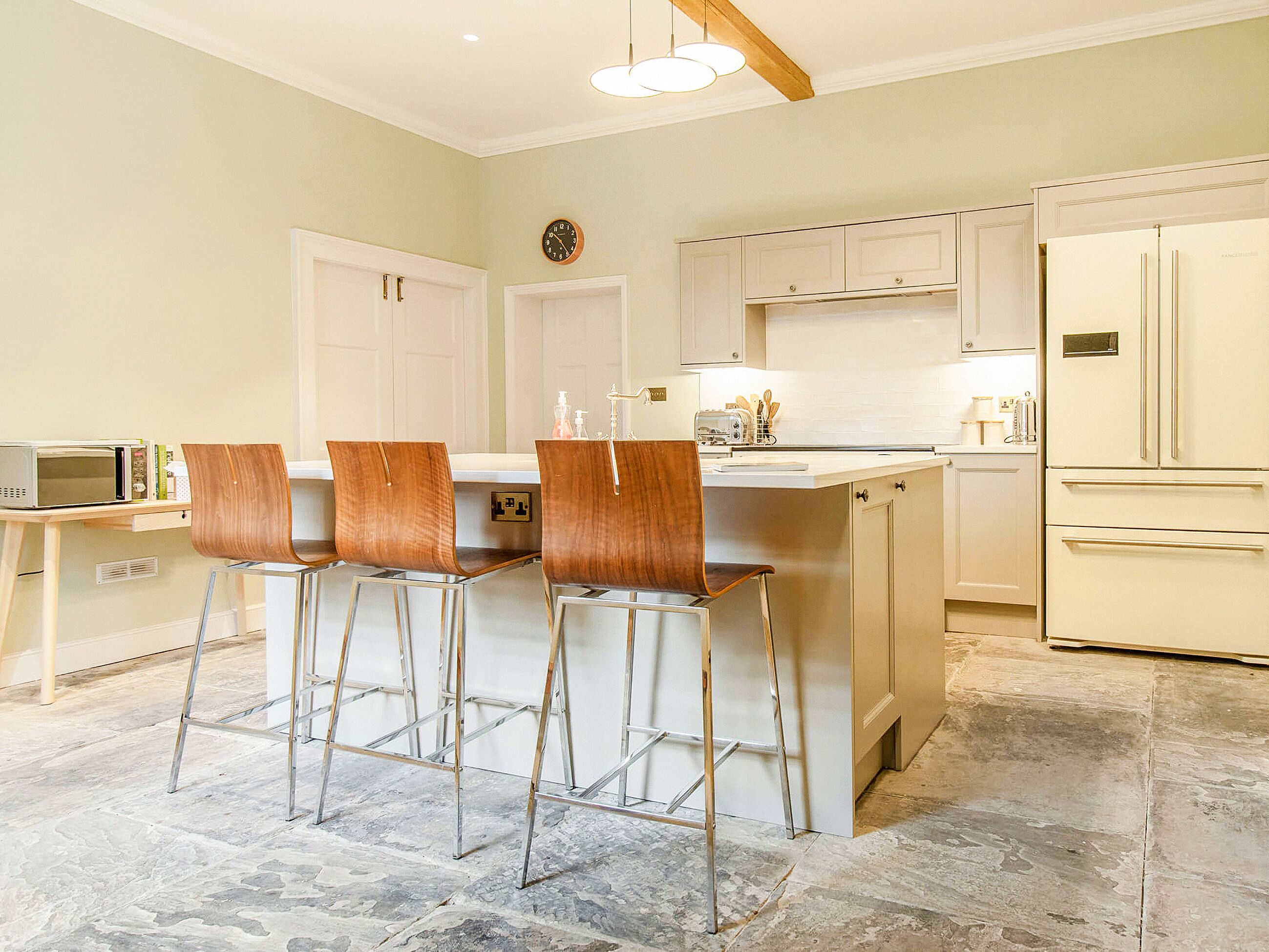 A kitchen with a central island, bar stools, a microwave, and a refrigerator.