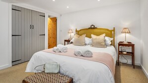 A neatly made bed with rolled towels, a wooden headboard, two bedside lamps, and a small wooden nightstand. - The Cwtch Apartment - Sea Views, Walk to Beach (Penally)