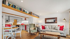 A modern living room with a sofa, coffee table, and a dining area with chairs and a table. - The Cwtch Apartment - Sea Views, Walk to Beach (Penally)
