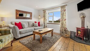 A cozy living room with a sofa, a coffee table, a fireplace, and a television mounted on the wall. - The Cwtch Apartment - Sea Views, Walk to Beach (Penally)