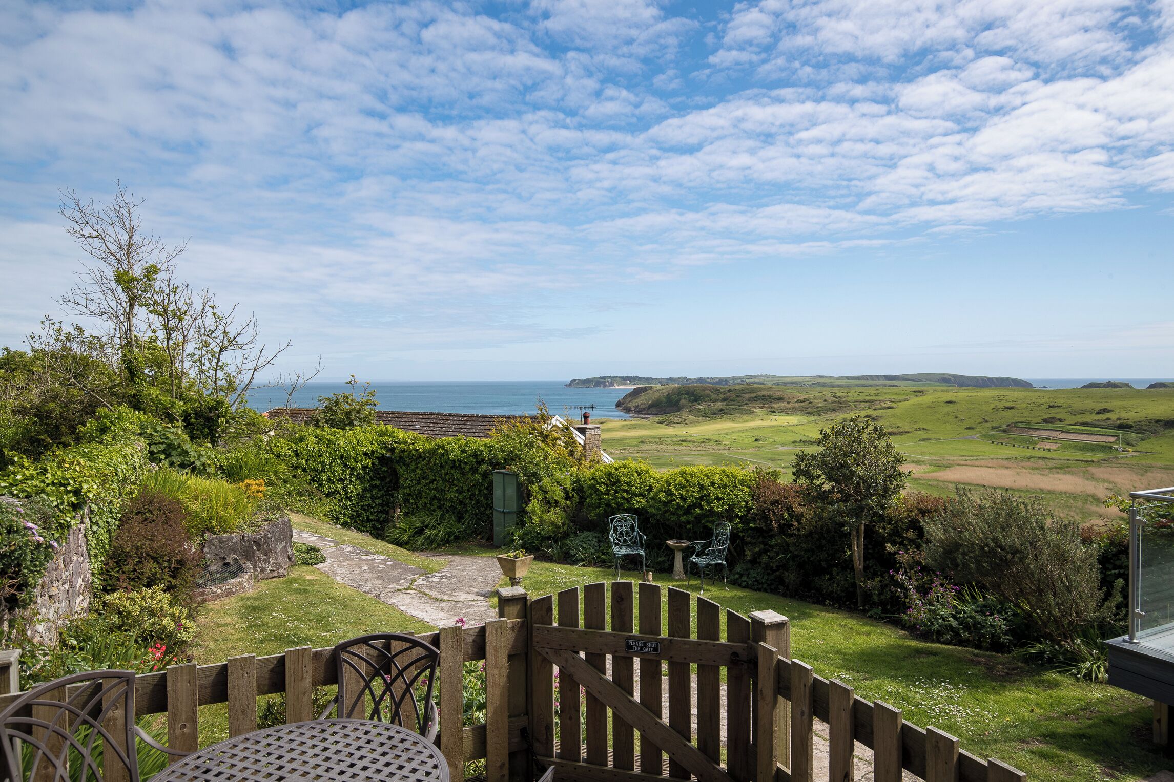 A patio with a view of the sea, a wooden gate, and a grassy landscape.