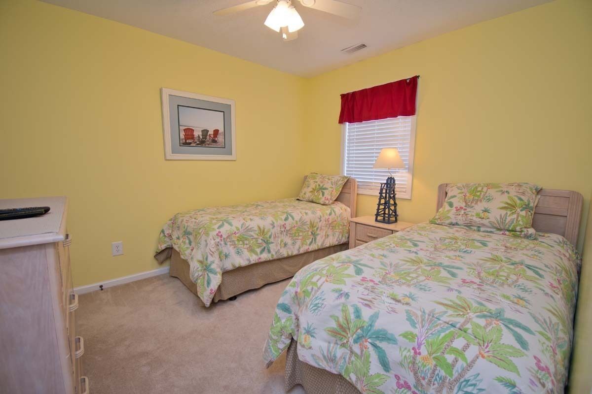 A bedroom with two beds, a nightstand, a lamp, and a ceiling fan.