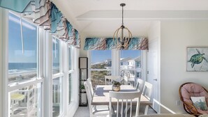 Una habitación iluminada por el sol con vistas al océano, una mesa de comedor con sillas, una silla de mimbre y un cuadro de una tortuga.