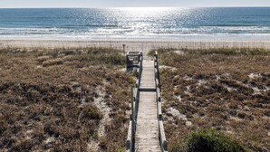 Un paseo marítimo de madera que conduce a una playa, con una cerca a lo lejos.