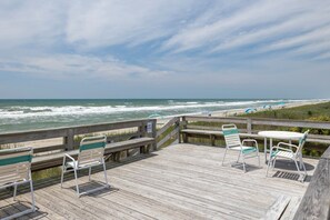 A wooden deck with chairs and a table overlooking the beach.