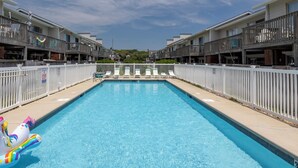 Ein rechteckiger Swimmingpool, umgeben von einem weißen Zaun, in einem Gebäude mit Balkonen.