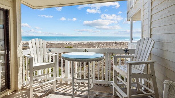 A balcony with two white Adirondack chairs and a small round table, overlooking a beach and ocean. - Point Emerald A-205, Oceanfront Condo in Emerald Isle, NC! (Emerald Isle)