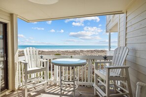 A balcony with two white Adirondack chairs and a small round table, overlooking a beach and ocean. - Point Emerald A-205, Oceanfront Condo in Emerald Isle, NC! (Emerald Isle)