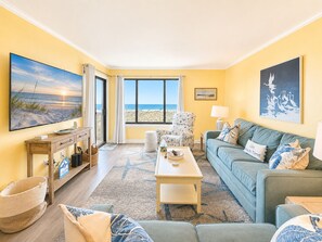 Sala de estar com vista para a praia, um sofá, uma mesa de centro e uma televisão.
