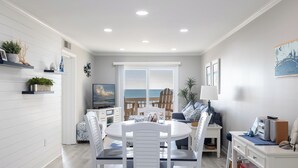 Een eetruimte met uitzicht op de oceaan, witte muren en een plafond met inbouwverlichting.