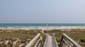 Een houten looppad dat naar een strand leidt, met een helder uitzicht op de oceaan.