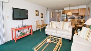 A compact living space with a sofa, a coffee table, a TV, and a kitchenette.