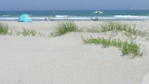 A beach with a tent and a person lying on the sand.