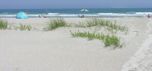 A beach with a tent and a person lying on the sand. - Point Emerald B-103, Almost Oceanfront Condo in Emerald Isle, NC! (Emerald Isle)