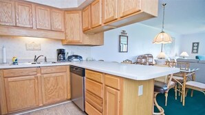 A kitchen with wooden cabinets, a dishwasher, a coffee maker, and a dining area with chairs and a table.
