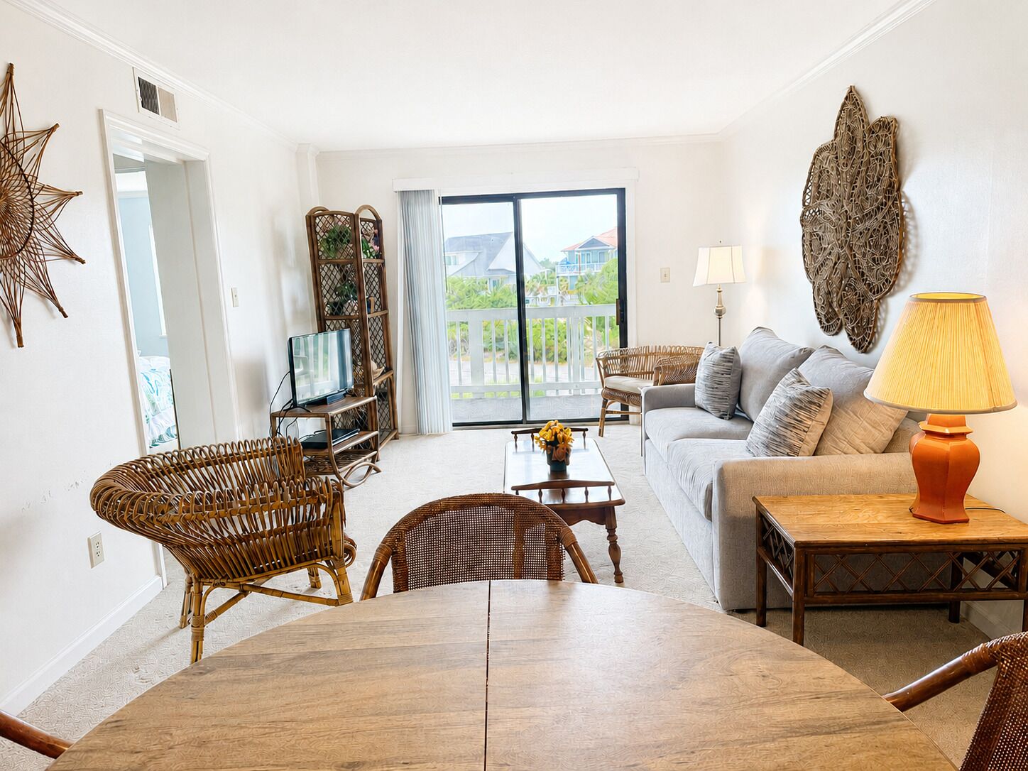 Ein Wohnzimmer mit einer Couch, einem Couchtisch, Korbstühlen, einem Fernseher und einem Balkon mit Blick.