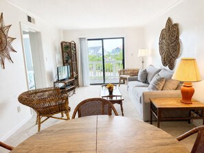 Un salon comprenant un canapé, une table basse, des fauteuils en osier, un téléviseur et un balcon avec vue.