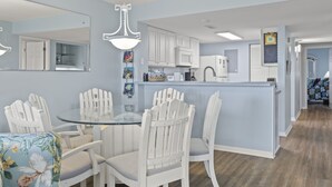 Une cuisine moderne avec des meubles blancs, un îlot central en verre et un coin repas comprenant des chaises blanches et une table en verre.