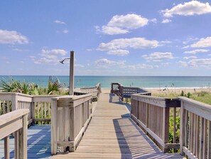 Ein hölzerner Steg führt zu einem Strand bei blauem Himmel.
