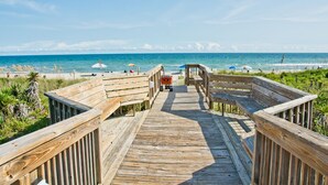 A wooden boardwalk leading to a beach with umbrellas and a clear view of the ocean. - Queens Court 1204, Oceanfront Condo in Emerald Isle, NC! (Emerald Isle)