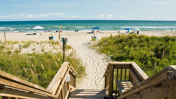 A wooden boardwalk leading to a sandy beach with umbrellas and people. - Queens Court 1204, Oceanfront Condo in Emerald Isle, NC! (Emerald Isle)