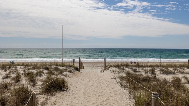 Ein Sandweg am Strand, der zum Meer führt, mit blauem Himmel.