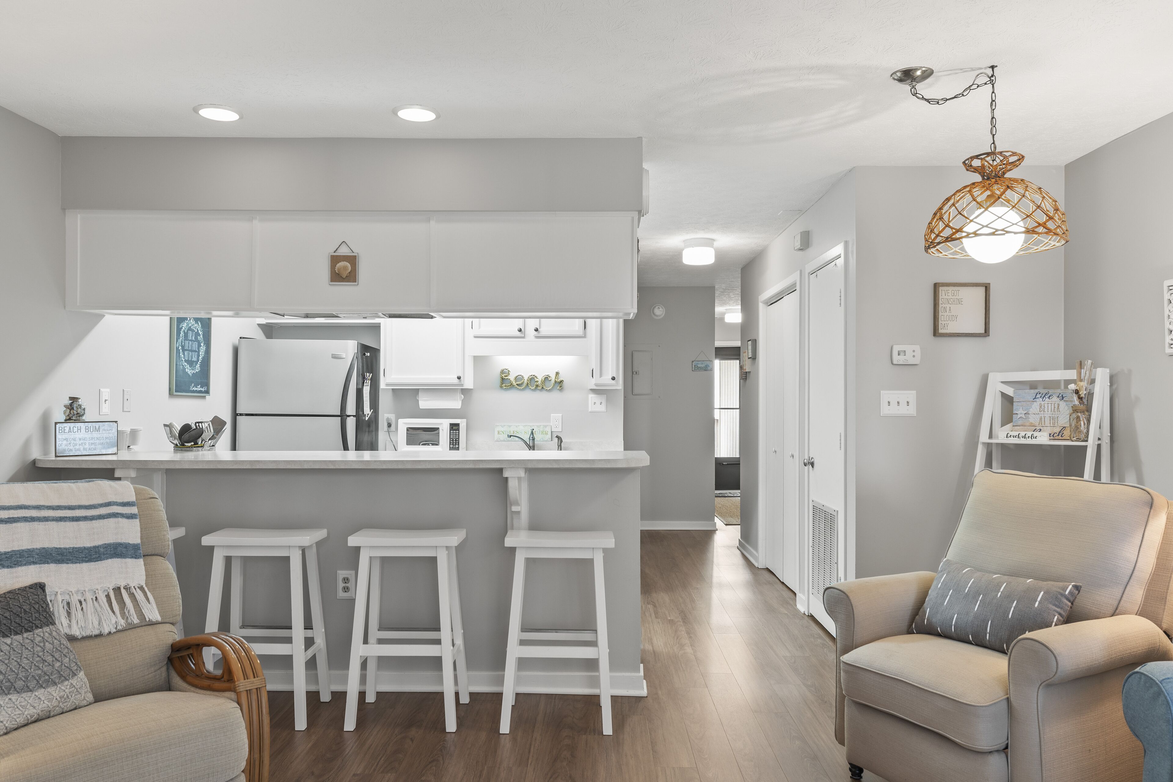 A modern kitchen with white cabinets, a central island with stools, and a hanging light fixture.
