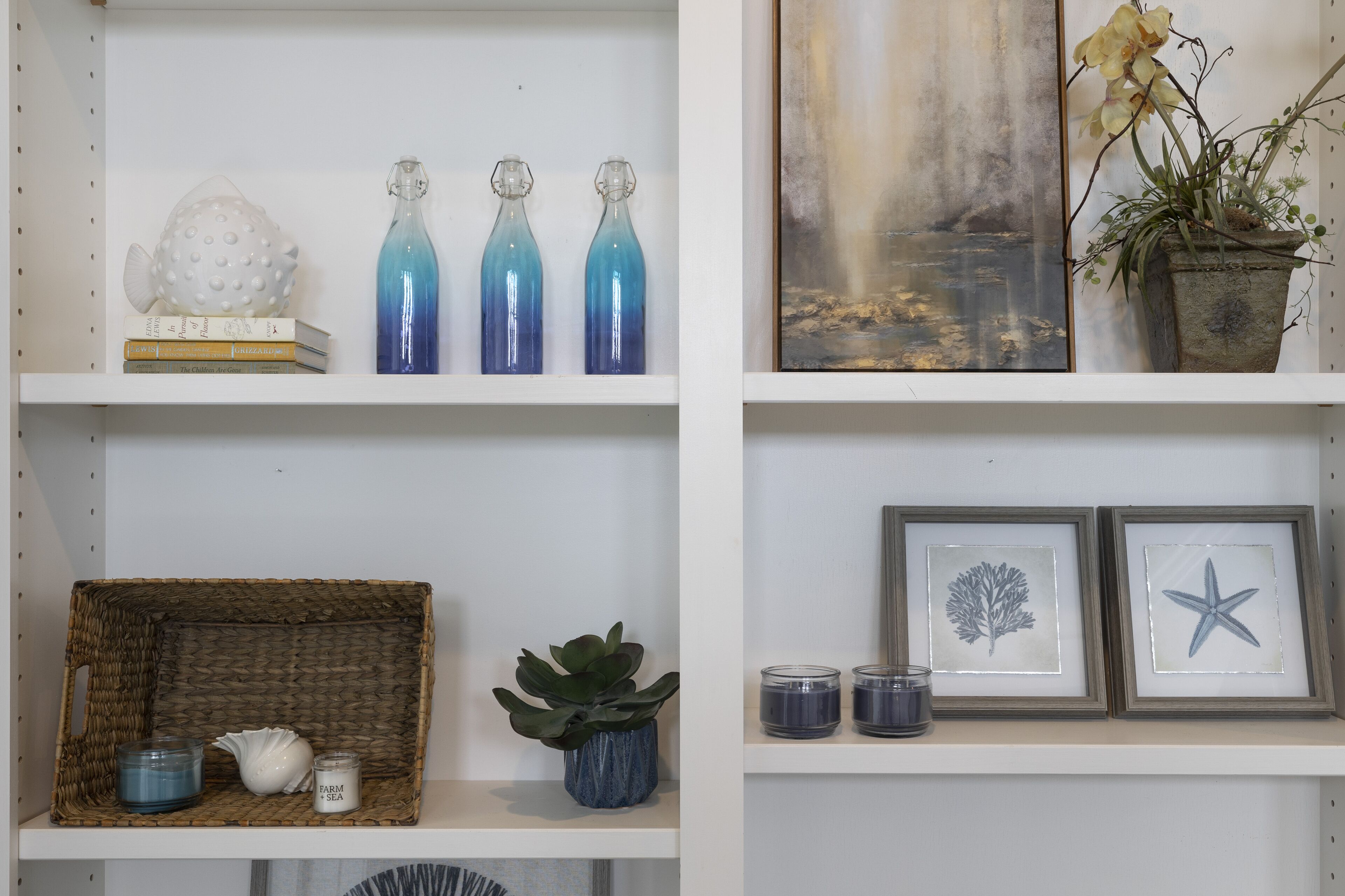 Una repisa con objetos decorativos, incluyendo botellas de vidrio, una escultura de pez, libros, una planta y fotografías enmarcadas.
