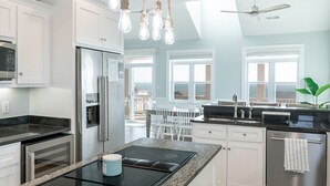 Una cocina moderna con armarios blancos, electrodomésticos de acero inoxidable, una encimera negra y vistas al exterior.