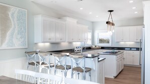 Una cocina moderna con armarios blancos, una isla central con taburetes y una lámpara colgante.