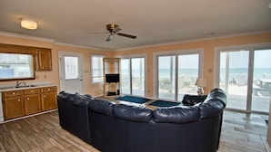 A spacious living area with a large dark leather sofa, wooden cabinets, and a view of the ocean through large sliding glass doors. - Red Roof Cottage East, Oceanfront Duplex in Emerald Isle, NC! (Emerald Isle)