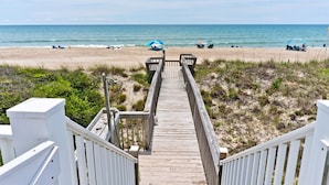 A wooden boardwalk leading to a beach with umbrellas and people. - Red Roof Cottage East, Oceanfront Duplex in Emerald Isle, NC! (Emerald Isle)
