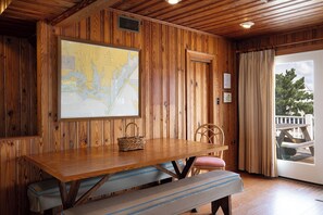 A wooden interior with a map on the wall, a wooden table, benches, and a view of the outdoors.