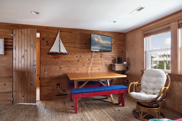 A wooden interior with a wooden table, a rocking chair, a bench, and a sailboat model on the wall. - Roberson Cottage, Oceanfront House in Atlantic Beach, NC! (Atlantic Beach)