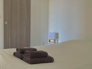 A hotel room with a bed, a wooden door, a nightstand with a lamp, and a window.