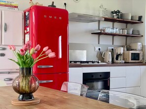 Une cuisine avec un réfrigérateur rouge, une machine à café, un four à micro-ondes et une cuisinière.